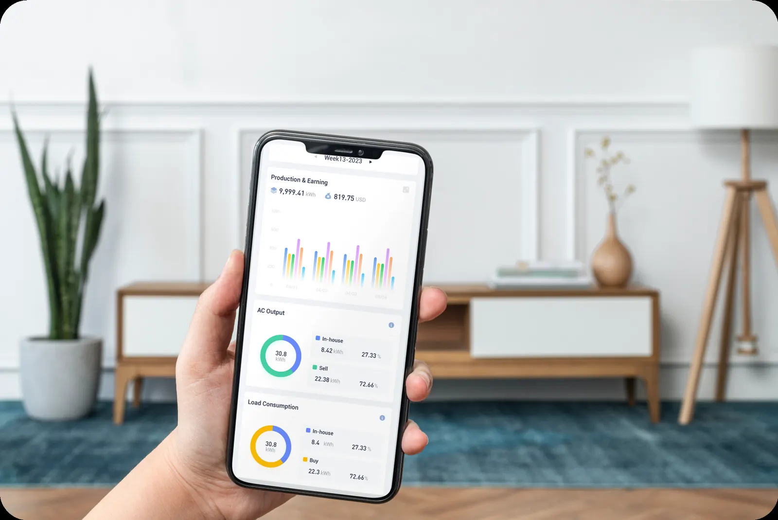 Hand holding a phone showing the GoodWe SEMS app with solar production, AC output and load consumption charts